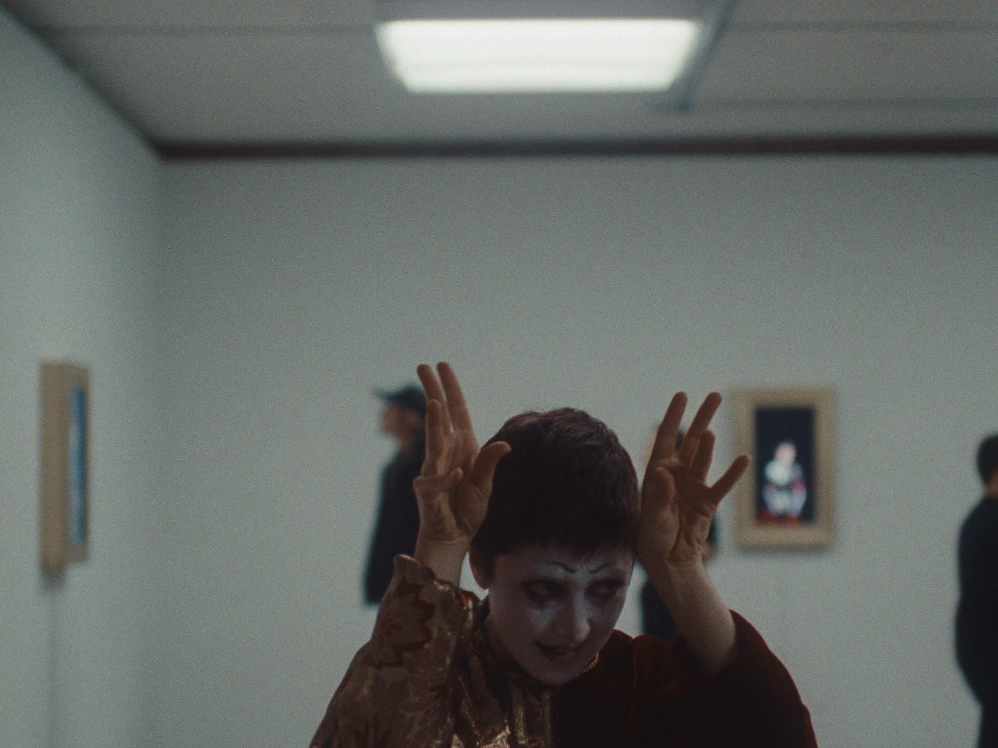 The short films protagonist, clad in their goth-mime makeup, is in art gallery and gesturing with both hands on their head. They almost appear to be attemping to scare someone